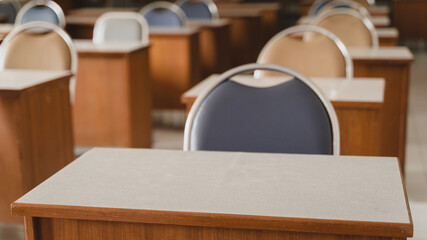 Many wooden tables and chairs well arranged in the university classroom but no student. Empty classroom with no student due to school being lockdown during COVID-19 pandemic.