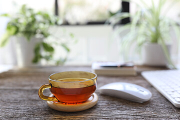 Tea in transparent glass cup on wooden table with mouse and keyboard