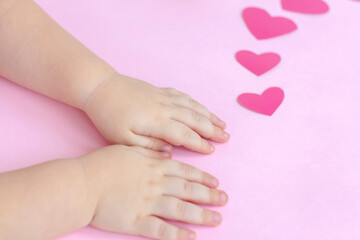 Obraz na płótnie Canvas Children's hands on a pink background with hearts. The concept of the Valentine's Day theme. A greeting card, a declaration of love.