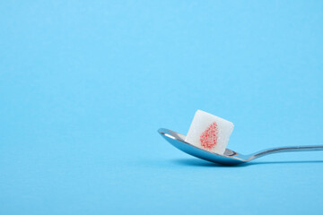 diabetes concept, sugar cube with drawn blood drop in metal spoon on blue background