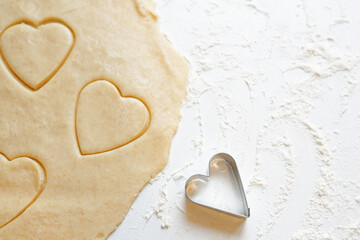 Hands pressing heart shaped cookie cutter into dough