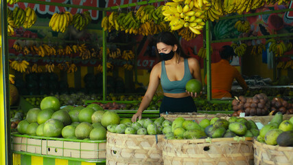 European girl in a black protective mask buys organic fruits in a store