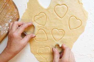 Hands pressing heart shaped cookie cutter into dough