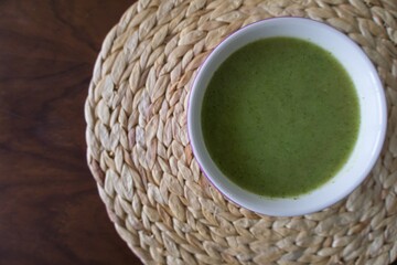 spinach and zucchini cream into a white bowl on natural fiber background. Healthy food concept