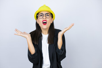 Young architect woman wearing hardhat clueless and confused expression with arms and hands raised