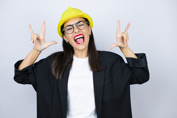 Young architect woman wearing hardhat shouting with crazy expression doing rock symbol with hands up