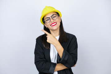 Young architect woman wearing hardhat smiling and pointing with hand and finger to the side