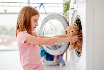Little girl putting toy into washing machine