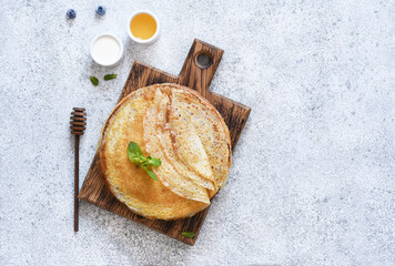 Thin pancakes with sour cream and honey on a wooden board on a concrete background. A stack of...