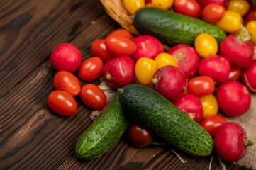 Green cucumbers, ripe radishes and colorful tomatoes scattered on the table. Close-up, selective focus.
