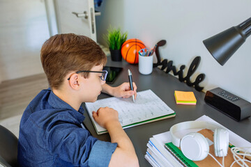 Left handed teenager doing homework on desk in his bedroom