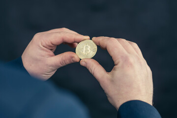 Virtual currency and blockchain concept. Businessman in a blue jacket holding Bitcoin in his hands.