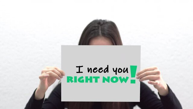 Conceptual message "I need you right now" on canvas frame label hold by beautiful girl smiling at camera