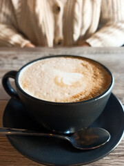 Close up black cup of coffee with shake milk on wooden table, sweather background, woman on background