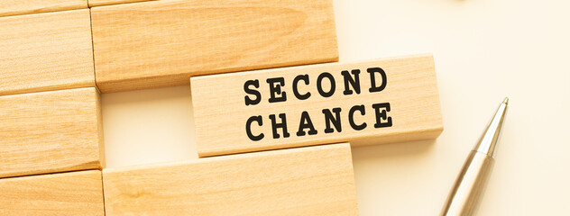 SECOND CHANCE text on a strip of wood lying on a white table with a metal pen.