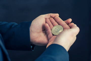 Virtual currency and blockchain concept. Businessman in a blue jacket holding Bitcoin in his hands.