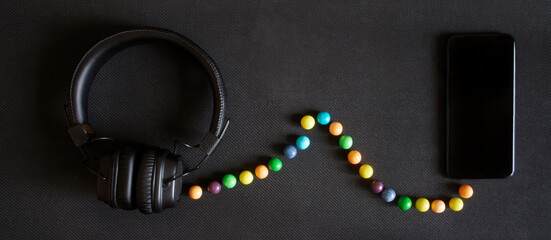 Headphones with ear pads and a smartphone lie on a black background. Multicolored balls simulate...