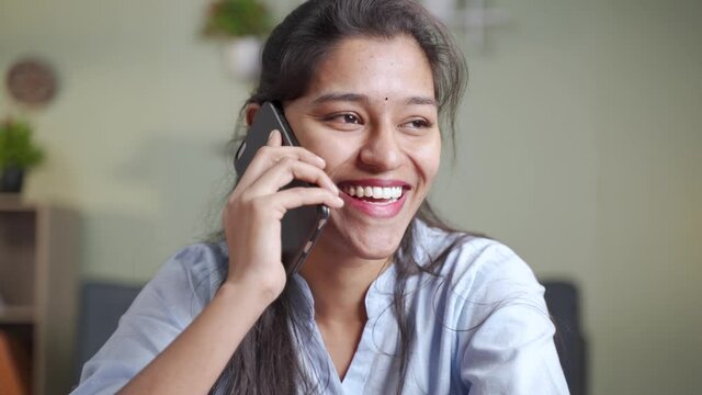 Close up head shot of happy Smiling young Indian business woman busy talking or having conversation on mobile phone call - concept of positive mood or emotion or doing doing time pass at work place