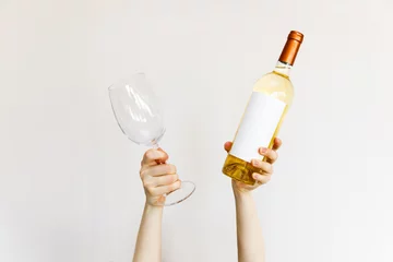 Rolgordijnen Human hands holding a wine glass and bottle of white wine on wall background. © Bostan Natalia