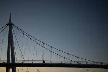 Siluetas de pareja caminando sobre puente colgante moderno al atardecer