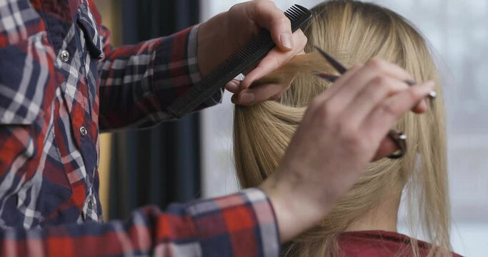 Hairdresser cutting blonde womens split and dry hair ends at home or salon.