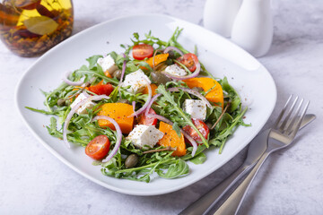 Warm salad with pumpkin, feta cheese, tomatoes, capers, arugula and red onion. Close-up.