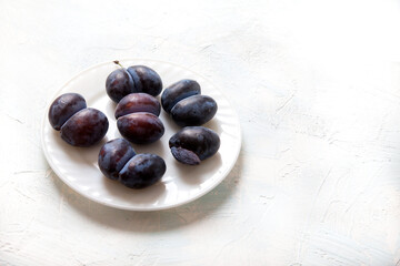 Ugly funny accrete plums lie on a white porcelain plate. Vegetarian food concept. Copy space.