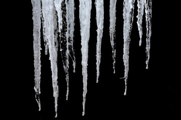 Icicles on black. Close-up. Textured background. Transparent clear icicles of various lengths and widths. The beauty of nature in the smallest detail