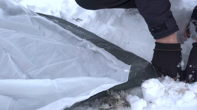 The hands of a person pushing tent pegs into snow