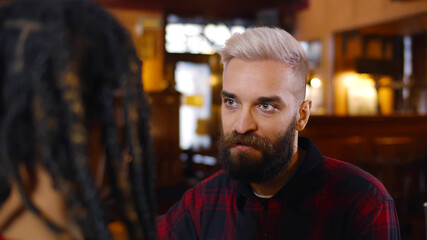 Portrait of hipster bearded man talking to african woman sitting in modern bar