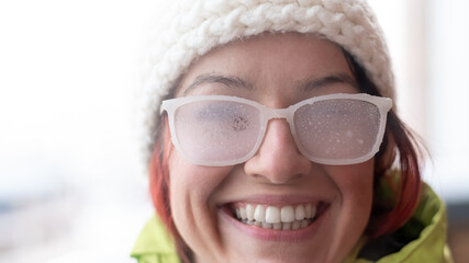 Caucasian woman with glasses smiling and freezing outdoors in winter.