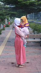 Portrait Asian muslim mother wearing hijab holding her child on the city park