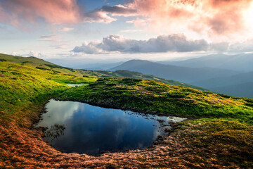 Mountain lake on sunrise time. Picturesque summer landscape with green mountain hills and sun rays in morning sky. Carpathian mountains