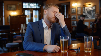 Sad young businessman drinking beer at pub relaxing after day at work