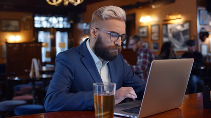 Young businessman drinking beer while using laptop in restaurant