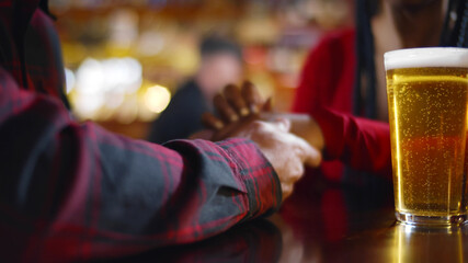 Close up of couple holding hands having beer sitting in bar