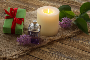 Obraz na płótnie Canvas Bottle of perfume, candle and lilac flowers on wooden background.