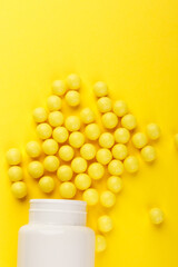 Yellow vitamin C capsules spilled out of a white jar against a Yellow background. Take care of your health. Vitamins and minerals. Free space