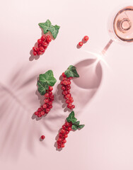 Beautiful red currant twigs in palm and wine glass shadow on a bright pink background. Fruit creative layout. Flat lay.