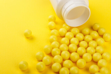 Yellow vitamin C capsules spilled out of a white jar against a Yellow background. Take care of your health. Vitamins and minerals. Free space