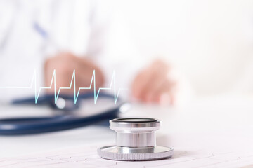 Gray stethoscope on cardiogram. Heart rate. Blurred doctor cardiologist in white uniform writes...