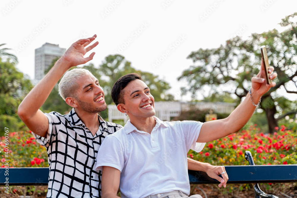 Wall mural Happy gay couple waving sitting on a bench in a park