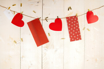 Red hearts and envelopes hanging on cord on wooden background. Postcards with love symbols on white wood with copy space. Horizontal backdrop with valentine themes.