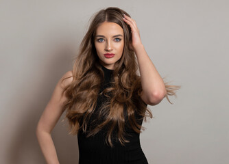 Fototapeta premium Beautiful young woman with long and healthy wavy hair posing in dress showing healthy figure and wearing wrist watch