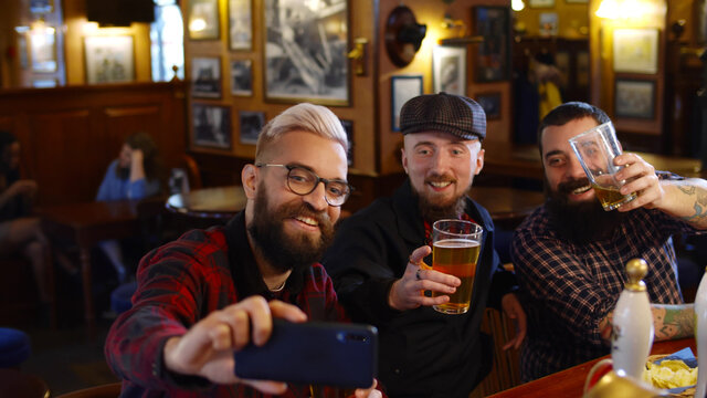 Group of young male friends taking selfies at beer pub.