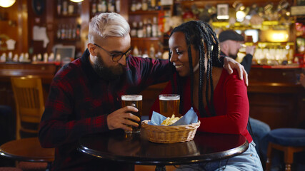 Diverse couple hugging having glass of beer in bar