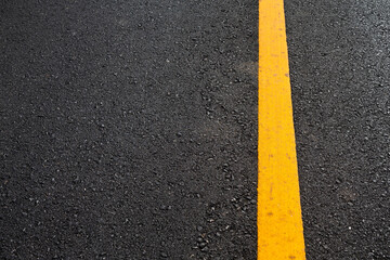 Close up black asphalt road surface texture with a yellow line.