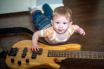 Infant baby rockstar playing music on bass guitar wearing vintage onesie and jeans great for music lessons, rock and roll, country music, future family financial planning