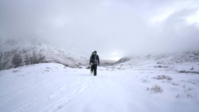 A man walking through deep snow in the mountains of Snowdonia in the UK