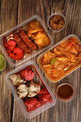 Top view of traditional Indian food in a plastic box on a wooden table. Indian fast food delivery at home. Eat at home.